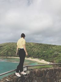 Woman looking at sea while standing on retaining wall by sea against sky