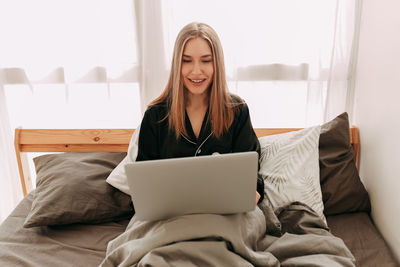 Smiling young woman using laptop on bed at home