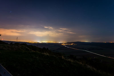 Road amidst illuminated land against sky at night