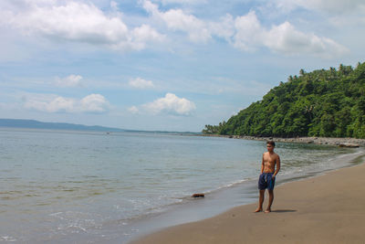 Shirtless man standing on beach against sky