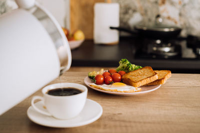 Homemade breakfast on the wooden table in the kitchen, blurred cup of coffee with kettle