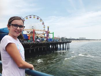 Portrait of man standing at amusement park by sea against sky