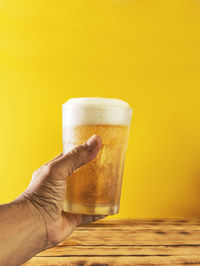 Close-up of hand holding beer glass against yellow background