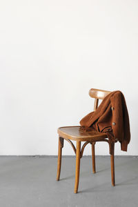 A knitted jacket made of brown woolen yarn lies on a wooden chair.