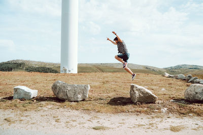 Man jumping on rock against sky