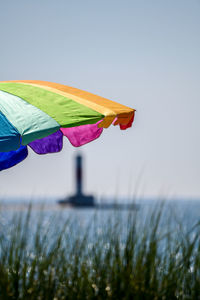 Close-up of multi colored umbrella against water and clear sky