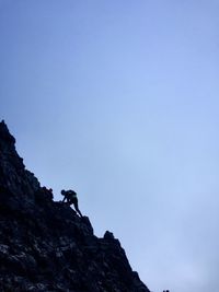 Low angle view of man climbing rocky mountains against clear sky