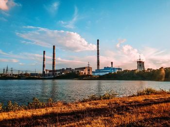 Factory by river against sky