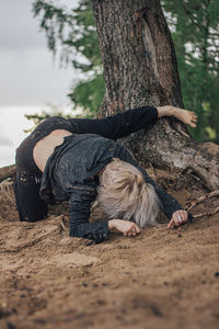 Young woman relaxing on sand at beach against sky