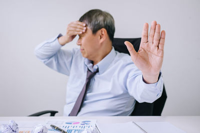 Businessman with headache sitting on chair while gesturing in office