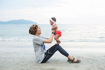 Rear view of mother and daughter on beach against sky