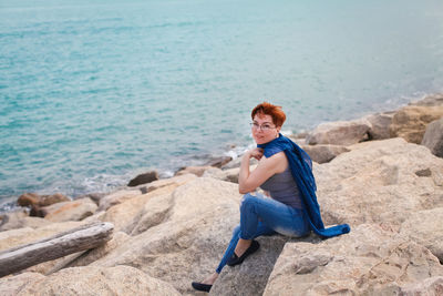 Full length of man sitting on rock at beach