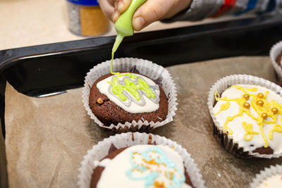 A child squeezes colored frosting from a tube onto chocolate brown cupcakes covered white frosting.