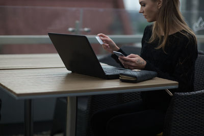 Young woman using laptop while sitting at sidewalk cafe