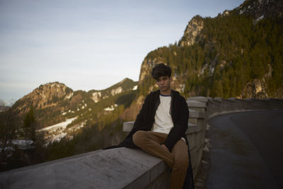 Man sitting on retaining wall against sky