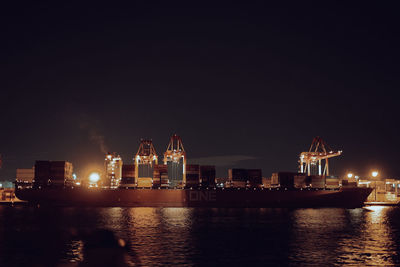 Illuminated buildings by river against sky at night