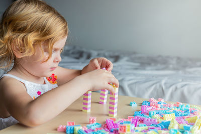 Little beautiful girl playing with toy plastic building blocks, sitting at the table. 