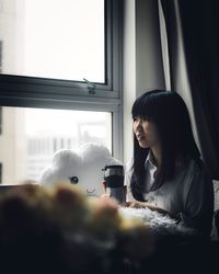 Woman sitting by window with drink at home