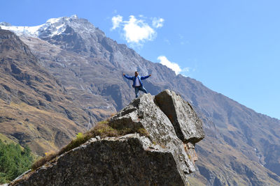 Man standing on rock by mountains against sky