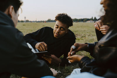 Young man holding book sitting with friends in park