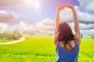 Rear view of woman with arms raised on field against sky