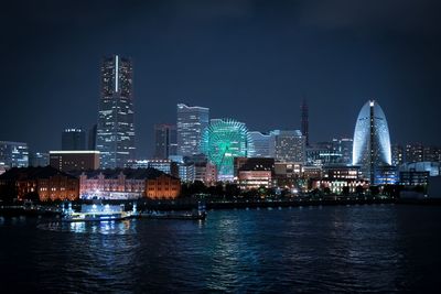 Illuminated buildings by river against sky in city at night