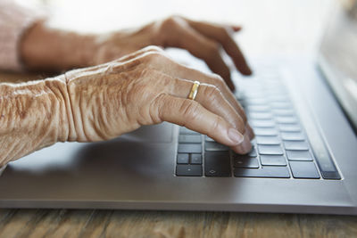 Hand of senior woman typing on keyboard of laptop, close-up