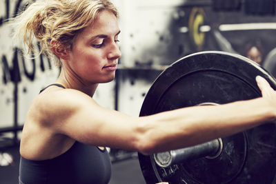 Young woman putting weight on barbell