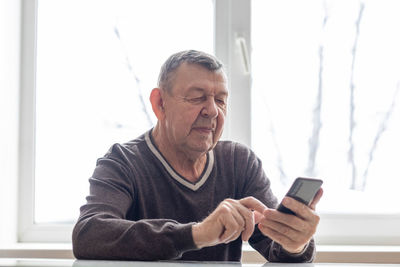 Elderly man dials number in smartphone from home. old senior sends sms on mobile phone