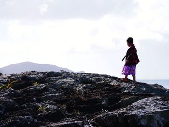 Side view of girl walking on rock against sky