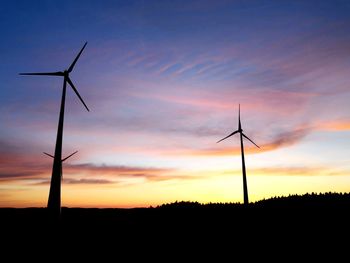 Silhouette wind turbines on field against sky during sunset