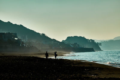 Silhouette people standing on beach against clear sky