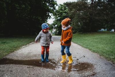 Male children jumping in the puddles at the park on rainy day