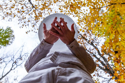 Low angle view of person hand against tree during autumn