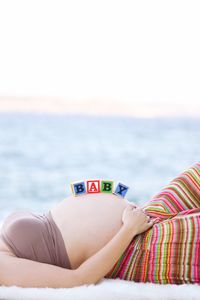 Midsection of pregnant woman with baby text relaxing by sea