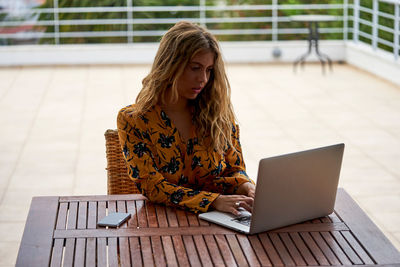 Young woman using phone while sitting on table