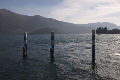 Wooden posts in sea against mountains