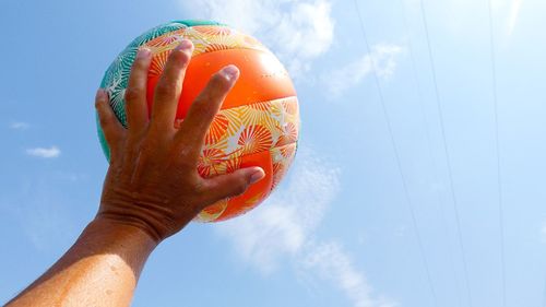 Low angle view of hand holding ball against sky