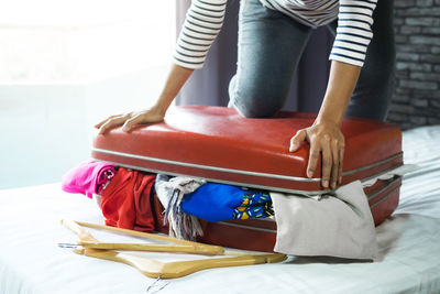 Midsection of woman packing suitcase on bed