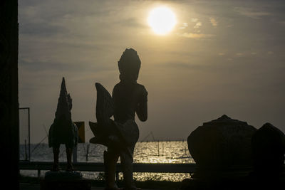 Silhouette people by sea against sky during sunset