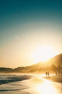 Scenic view of sea by mountain against clear sky during sunset