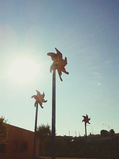 low angle view, sculpture, sky, statue, street light, art and craft, sunlight, sun, art, clear sky, blue, sunbeam, creativity, human representation, animal representation, built structure, lighting equipment, architecture, building exterior, lens flare