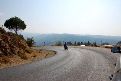 Rear view of man riding scooter on road against clear sky