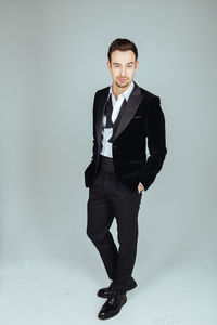 Portrait of confident young man in suit standing against blue background