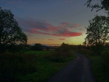 Road amidst field against sky during sunset