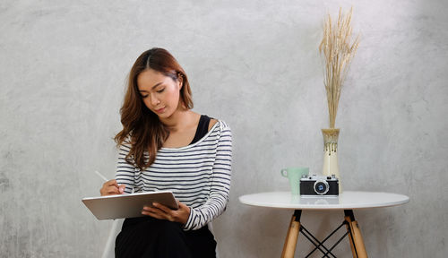 Woman using digital tablet while sitting against wall