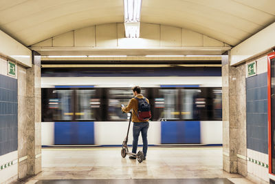 Man in stylish outfit waiting for the metro with electric scooter in the underground