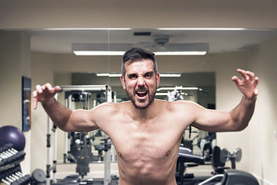 Portrait of angry shirtless young man screaming while standing in gym