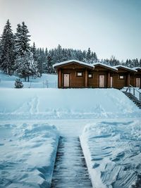 Snow covered house by building against sky