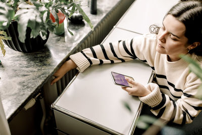 High angle view of woman checking temperature of radiator through smart phone application at home